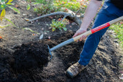 Photo of a person using a CRAFTSMAN garden hoe, SKU CMXMLTP35325, with wood handle, cultivating soil in a garden.