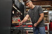 A person accessing a tool chest drawer in a workshop, with various tools and supplies organized in the background.